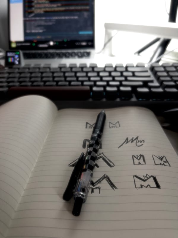 Photo of desk with laptop in the background and notebook, pen and keyboard.